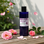 Plastflaska med MacUrth Vildros shampoo omgiven av färska vildrosblommor och kronblad på träyta, varmt ljus och mjuka skuggor